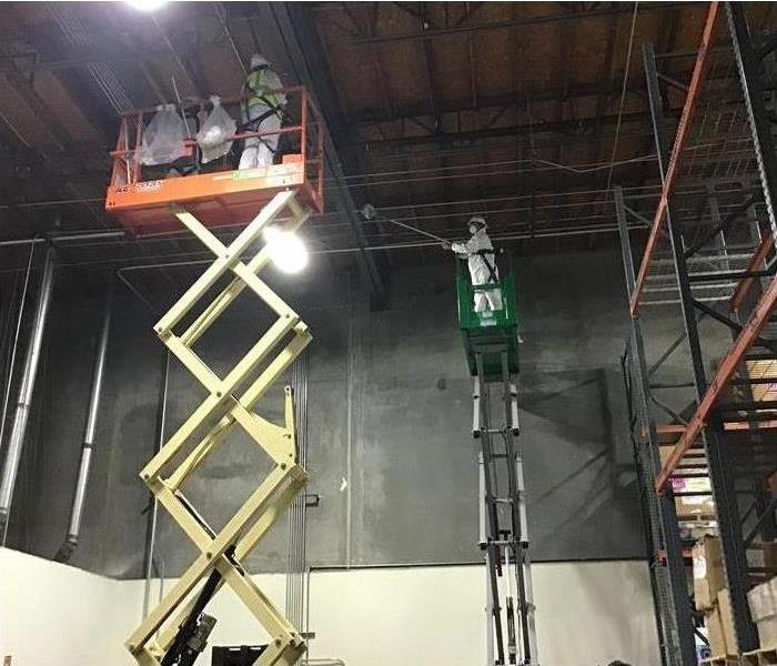 Two forklifts raised up to ceiling to clean
